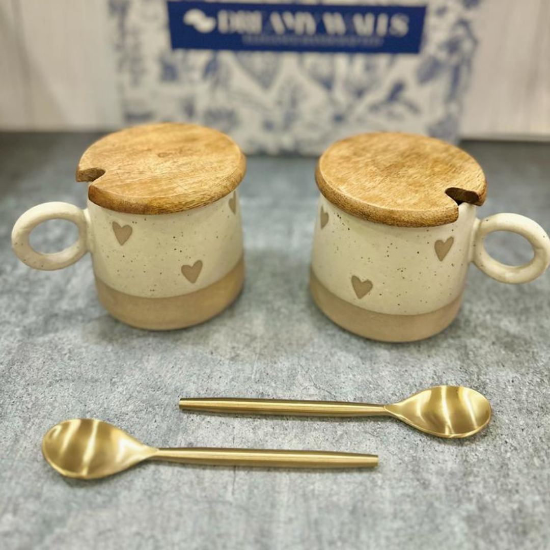 Two ceramic mugs with beige and white tones, adorned with small heart patterns, each topped with a wooden lid featuring a notch