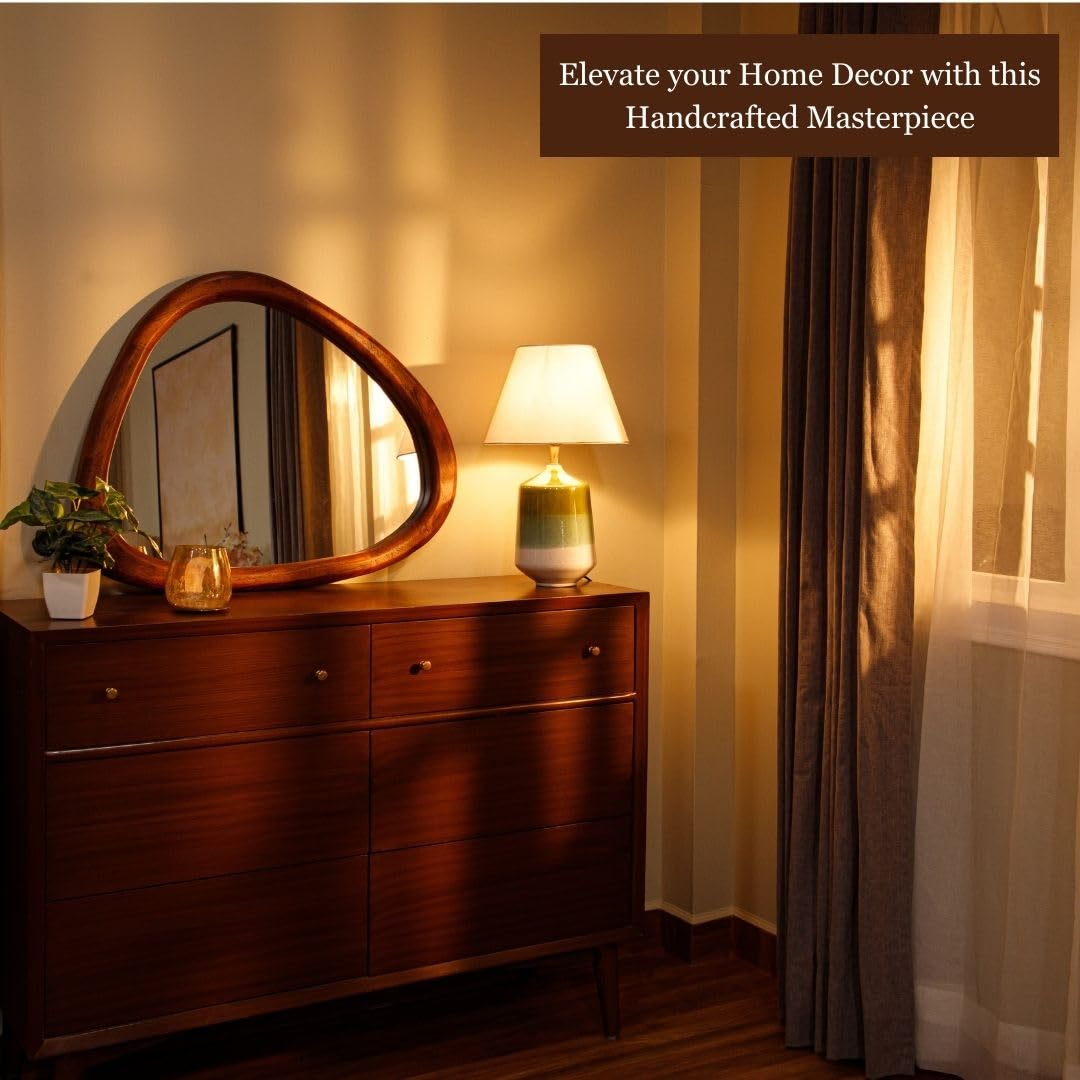 Wooden-framed asymmetrical mirror above a wooden dresser, styled with a white vase and a lamp