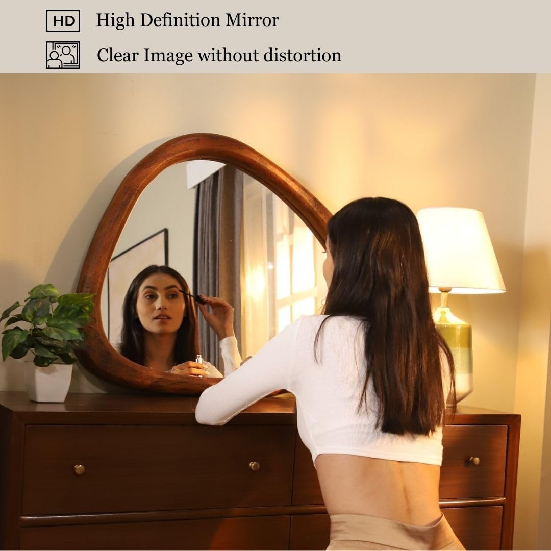 Wooden-framed asymmetrical mirror above a wooden dresser, styled with a white vase and a lamp