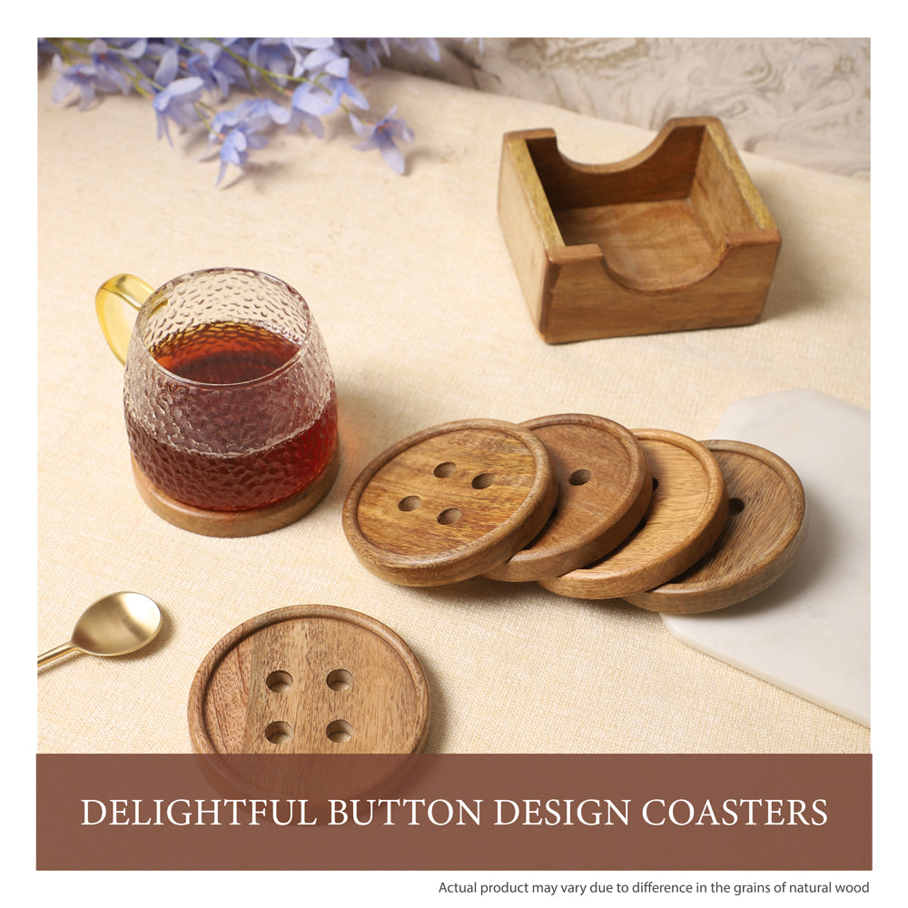 Wooden coasters with button-inspired designs and a matching holder, paired with a textured glass mug of tea and a golden spoon on a neutral tabletop