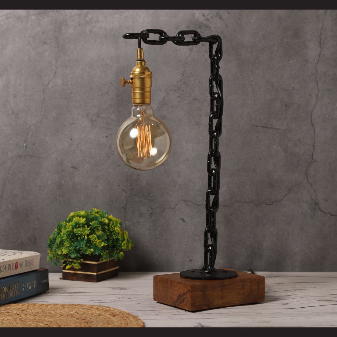 Industrial table lamp with black chain design, brass bulb holder, rosewood base, and decorative setup including books and greenery
