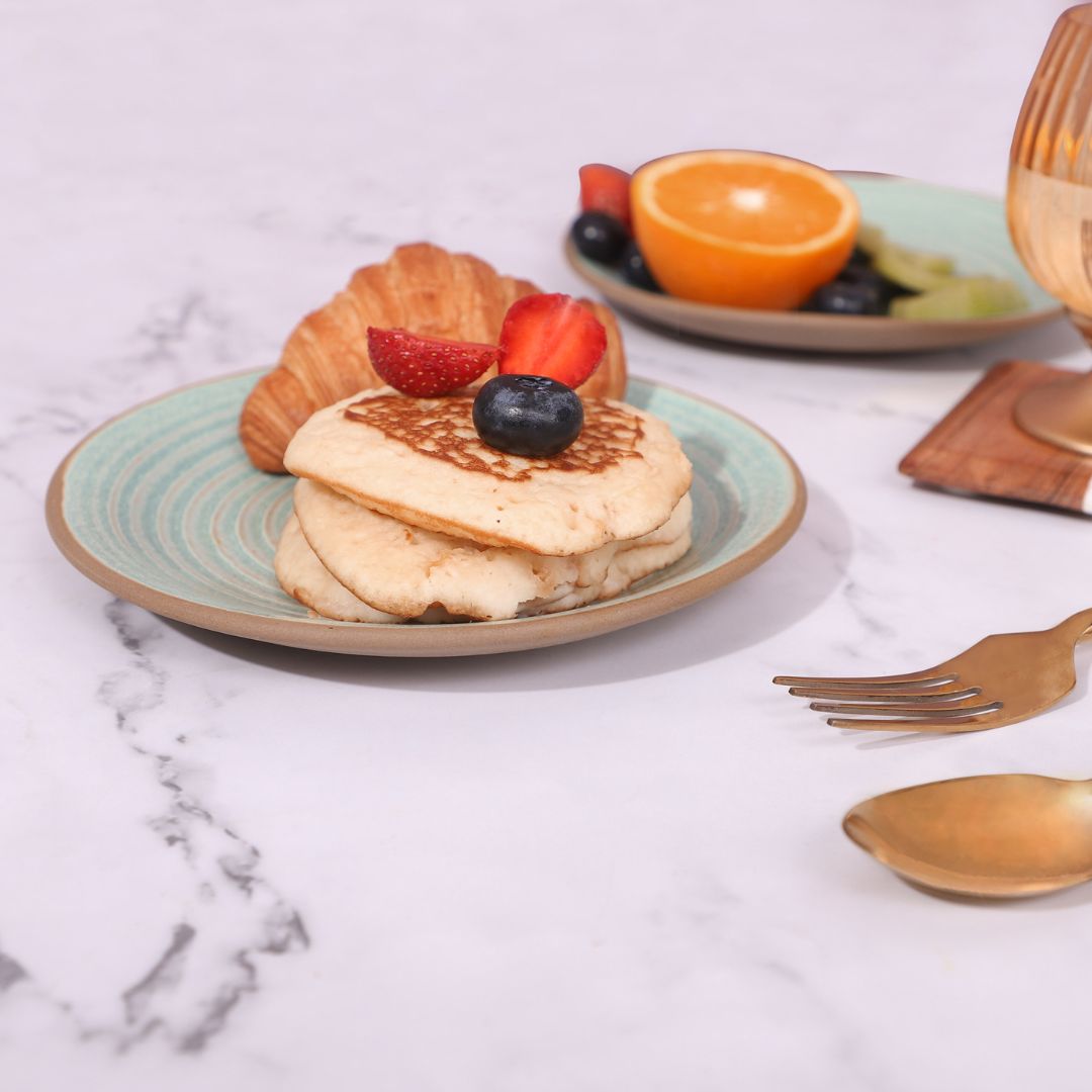 Set of two quarter plates with food, featuring a croissant and pancakes on one plate, and fresh fruits .