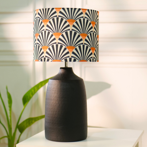 Modern table lamp with a patterned shade and a sleek black base, placed on a white surface near a green plant