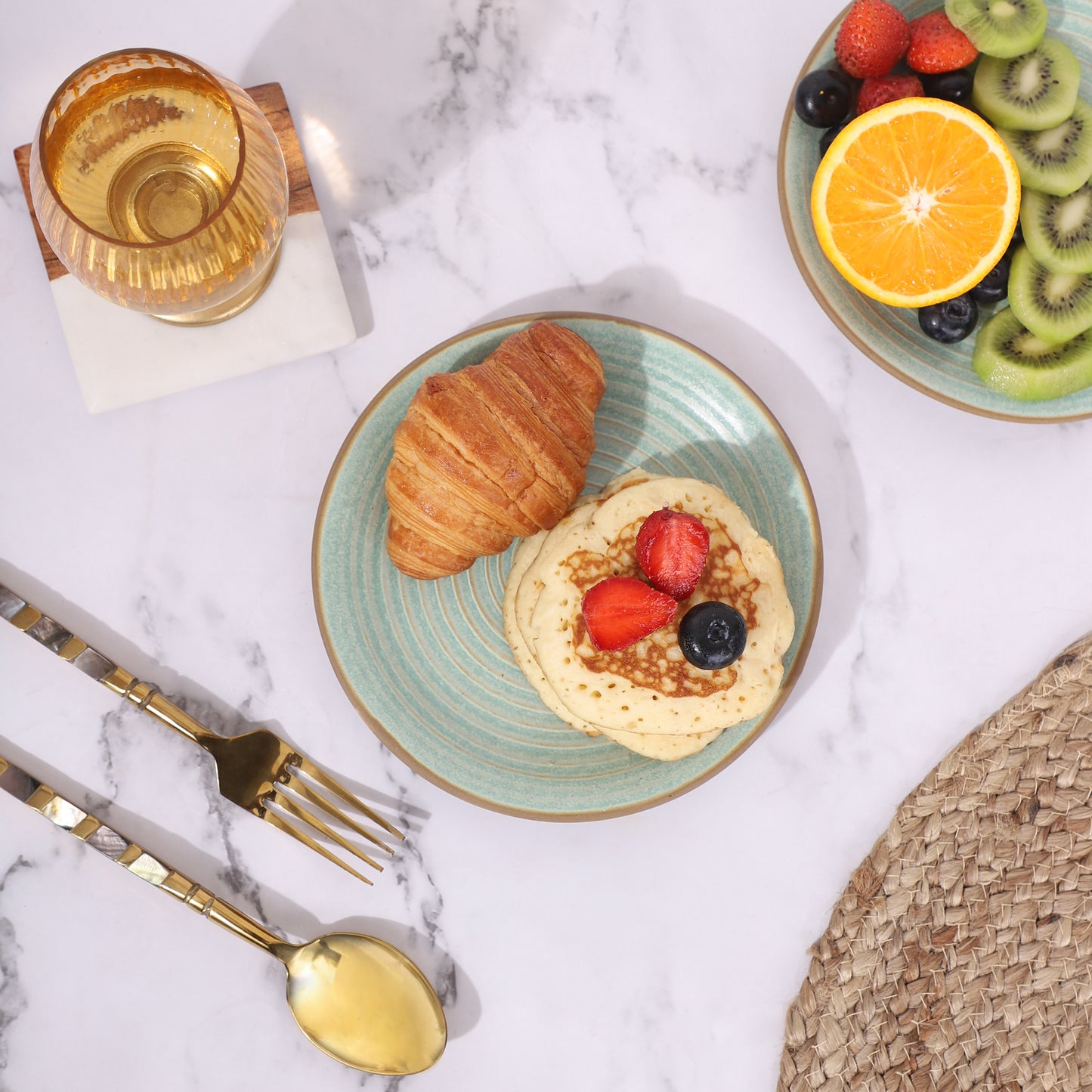 Set of two quarter plates with food, featuring a croissant and pancakes on one plate, and fresh fruits like kiwi, orange, and berries on the other.