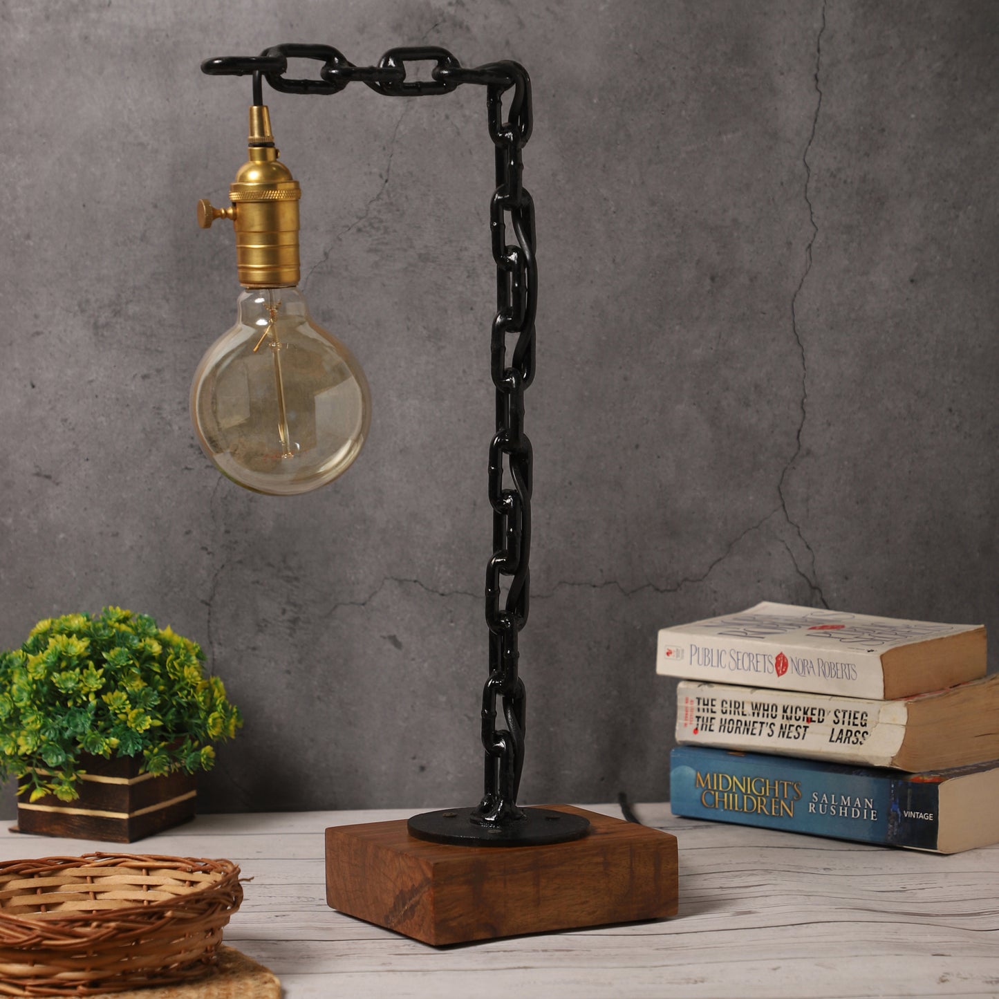 Industrial table lamp with black chain design, brass bulb holder, rosewood base, and decorative setup including books and greenery