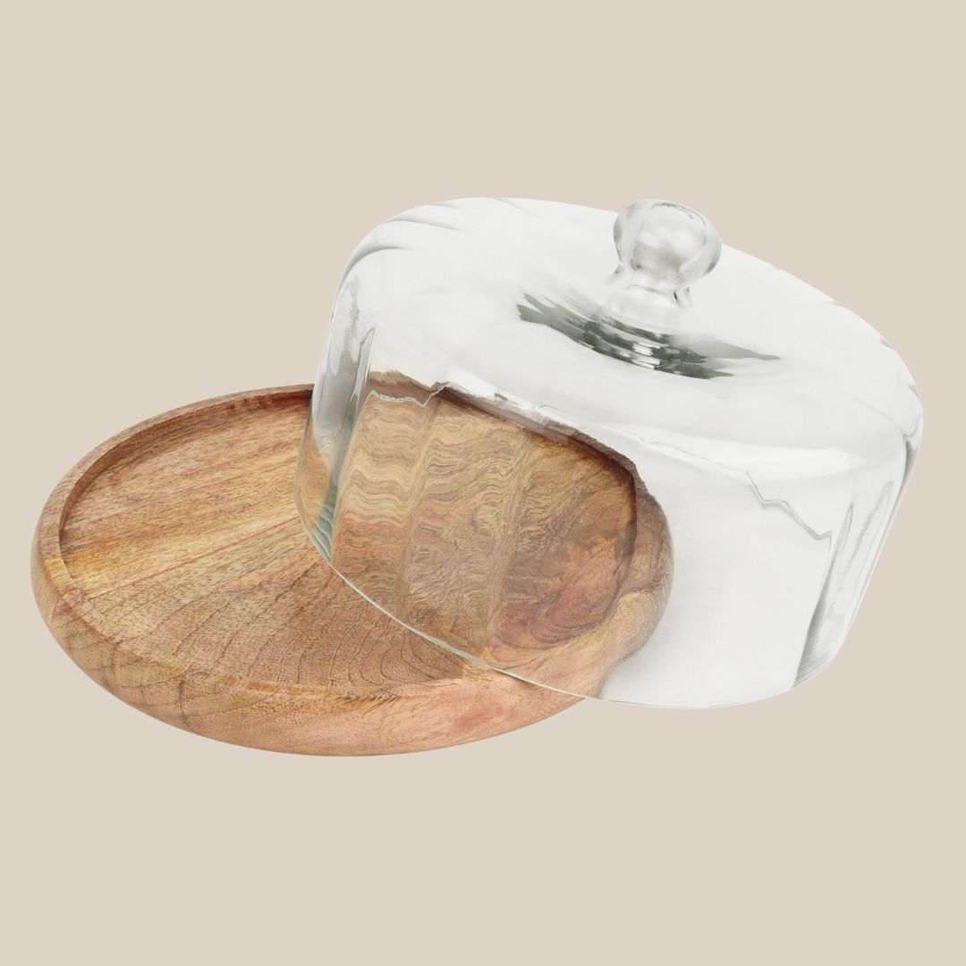 Transparent glass dome with a knob handle placed beside a round wooden serving tray on a beige background