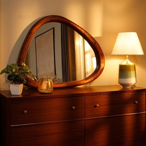 Wooden-framed asymmetrical mirror above a wooden dresser, styled with a white vase and a lamp