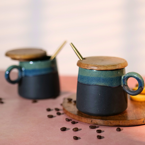 Two ceramic mugs with wooden lids and metal straws, placed on a wooden coaster with scattered coffee beans in the background