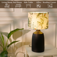 Table lamp with a dark, textured metal base and a floral-patterned fabric shade, placed on a white table in a room with plants — thumbnail