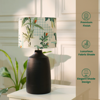 Table lamp with a dark, textured metal base and a floral-patterned fabric shade, placed on a white table in a room with plants — thumbnail