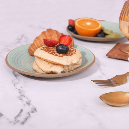 Set of two quarter plates with food, featuring a croissant and pancakes on one plate, and fresh fruits .