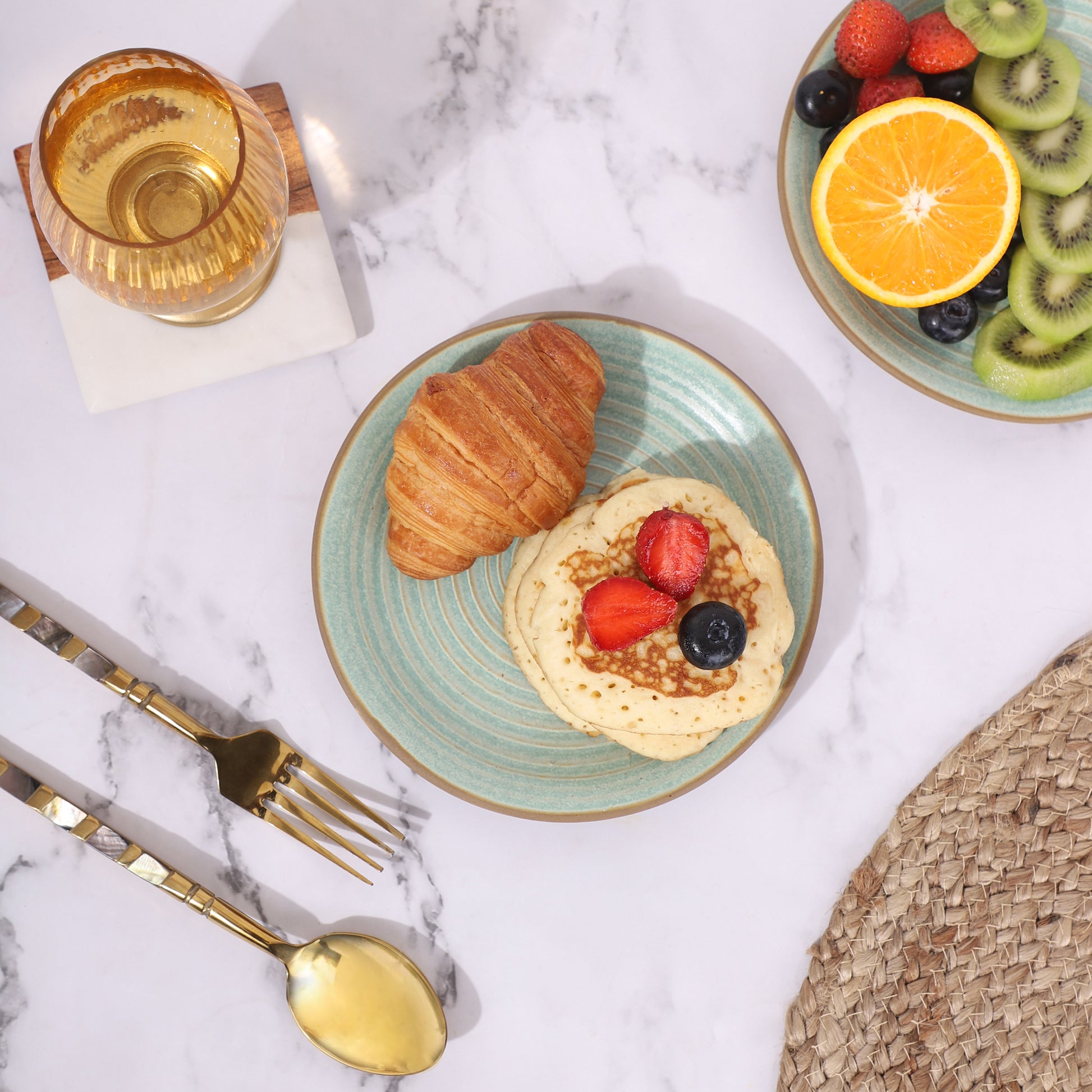 Set of two quarter plates with food, featuring a croissant and pancakes on one plate, and fresh fruits like kiwi, orange, and berries on the other. 