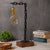 Industrial table lamp with black chain design, brass bulb holder, rosewood base, and decorative setup including books and greenery