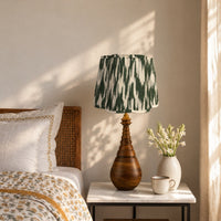 Hara Ikat scalloped lamp shade on the carved wooden teardrop table lamp by a bed, morning light — thumbnail